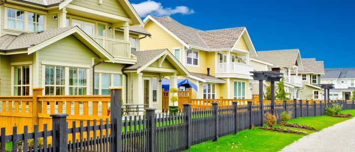 Housing lined up with a short fence lining the bright green grass on a summer day
