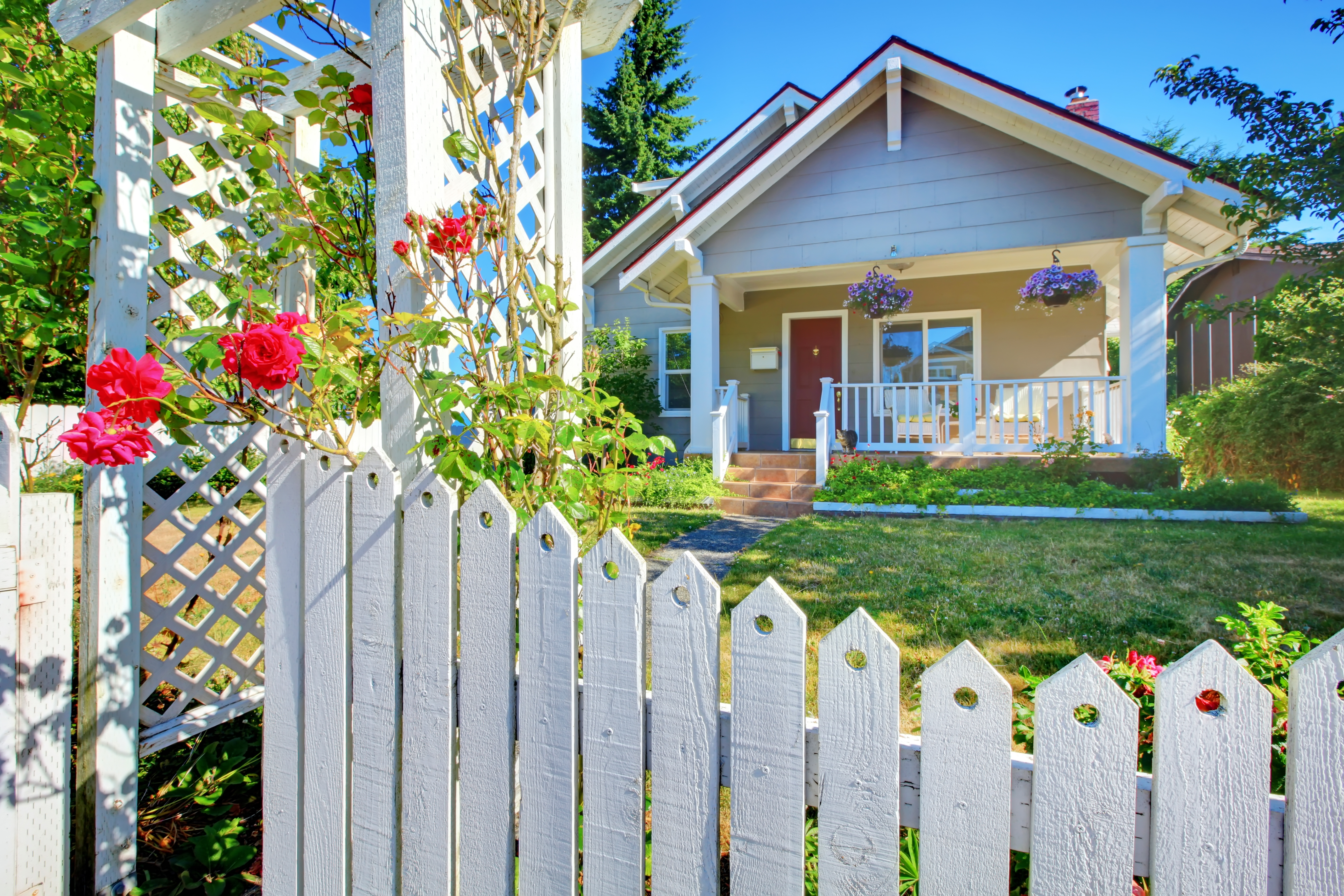 House tucked behind a beautiful white picket fence and green grass and flowers.