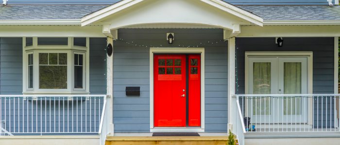 Close up photo of blue-gray home with red door and stairs leading to the entrance