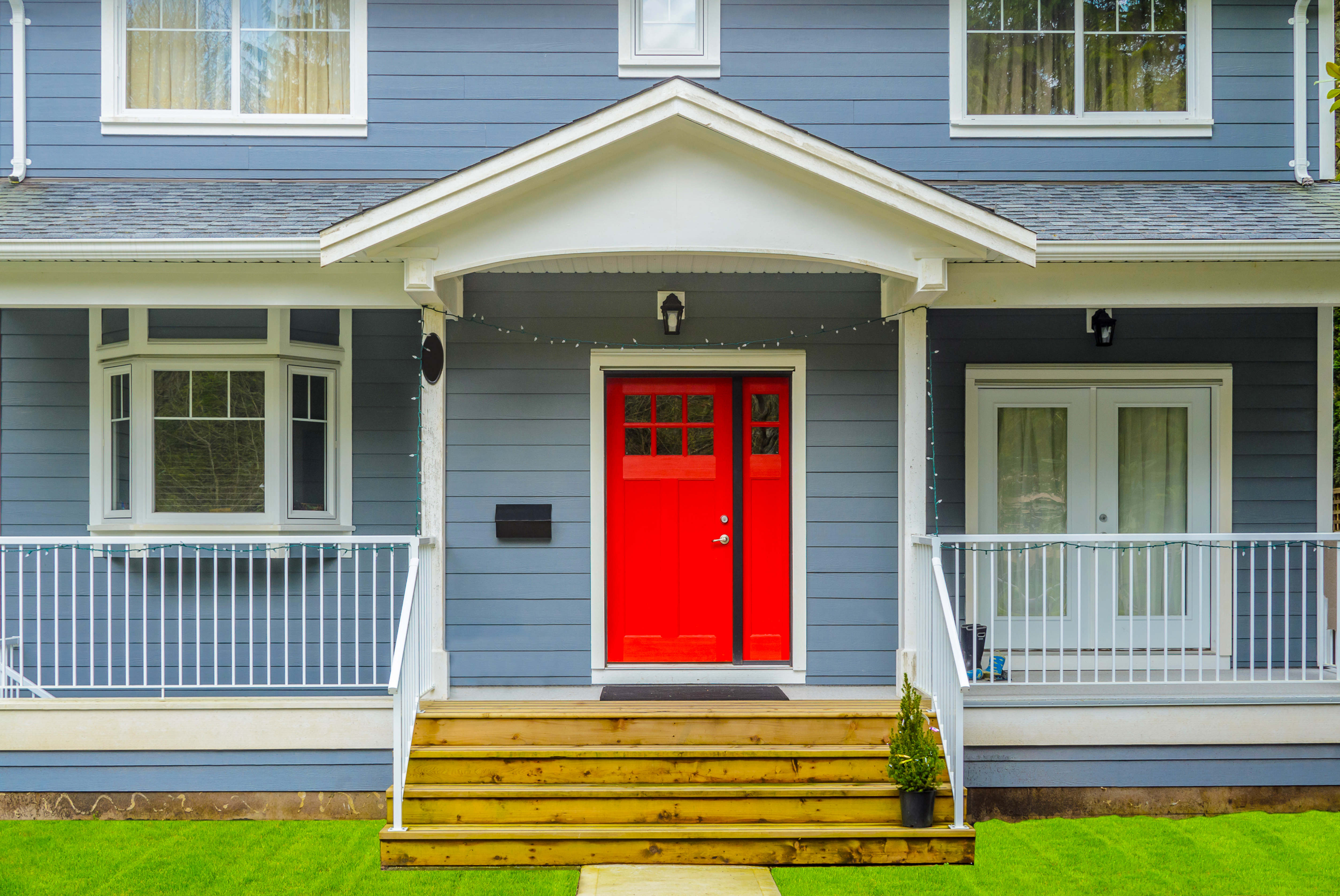 Close up photo of blue-gray home with red door and stairs leading to the entrance