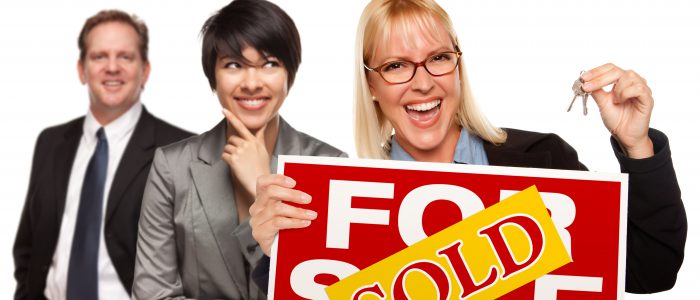 Real Estate Team Behind with Blonde Woman in Front Holding Keys and Sold For Sale Real Estate Sign Isolated on a White Background.