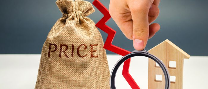 Money bag with word price, down arrow and wooden house. The concept of falling property prices. Lower housing prices. Low rent. The decline in the value of the property. Low utility prices