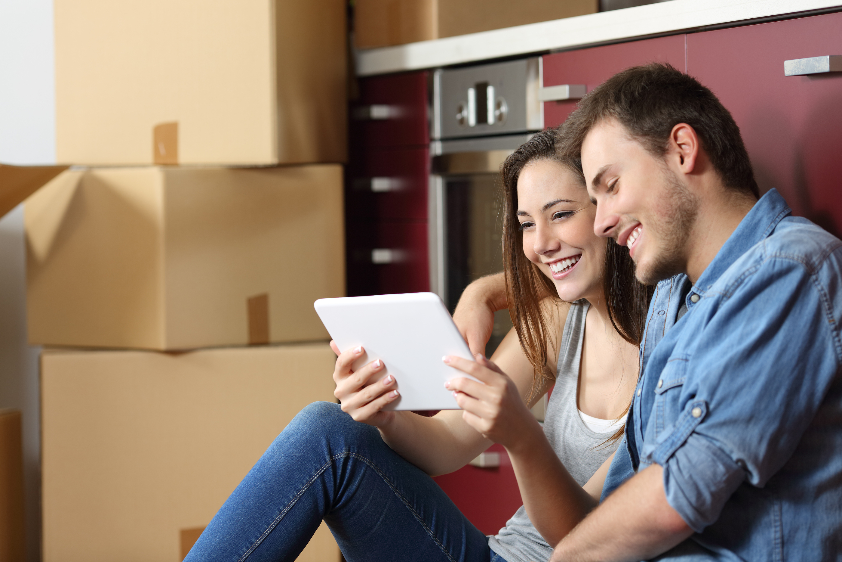 Couple sitting on the floor of the kitchen and buying online with a tablet and moving home