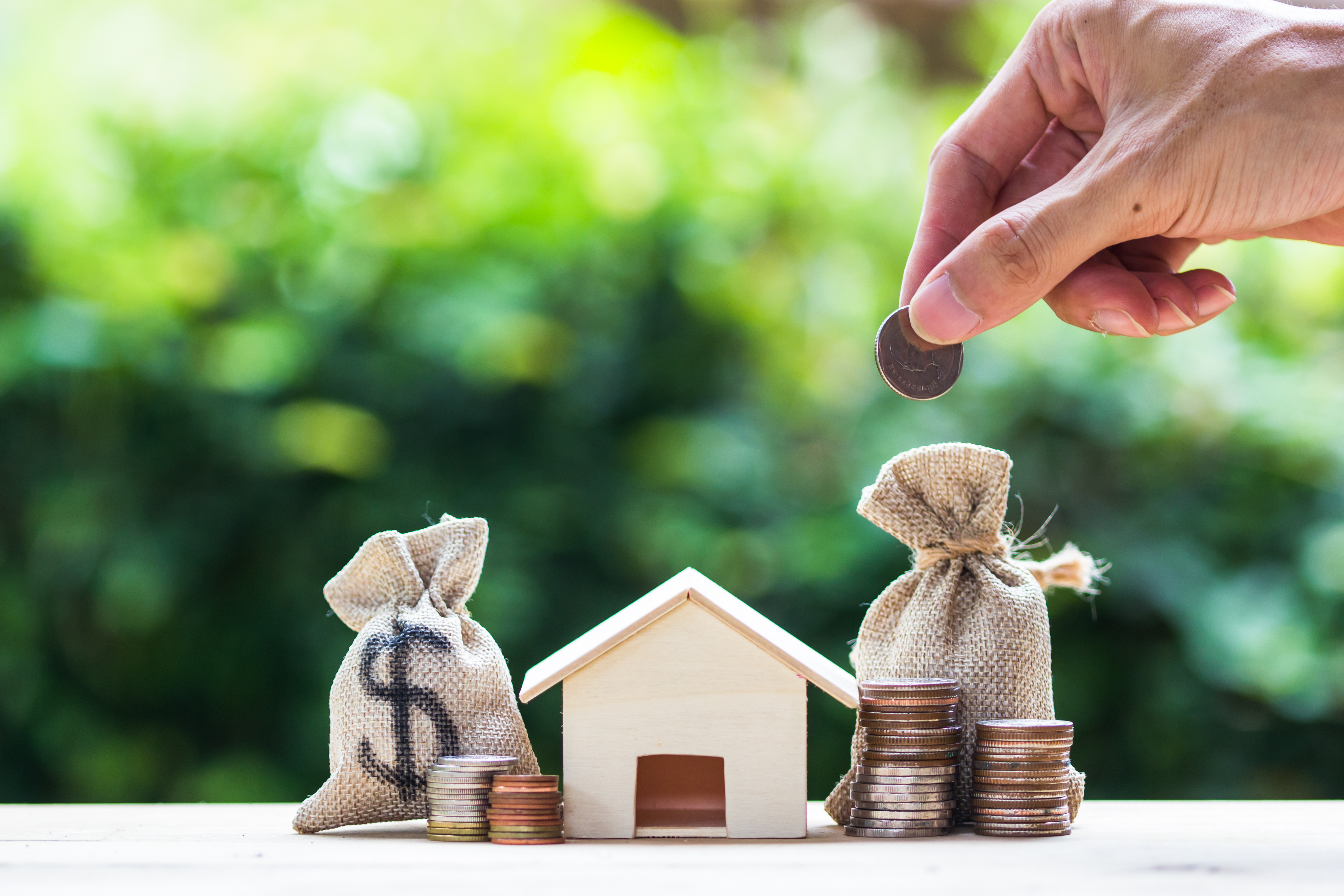 Saving money, home loan, mortgage, a property investment for future concept : A man hand putting money coin over small residence house and money bag